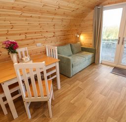 A wooden interior room with a dining table and chairs next to a green sofa and glass doors at Lloyd in Penzance near Newlyn