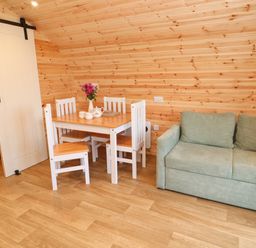 A small dining area with a wooden table and four chairs next to a green sofa and a bedroom with a bed behind a sliding door at Lloyd in Penzance near Newlyn