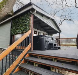 A raised wooden deck with stairs leading up to a covered area with a hot tub and outdoor seating surrounded by trees at Mill View in Dungiven Londonderry