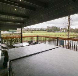 A covered balcony with a hot tub and a table with chairs overlooking a grassy field at Mill View in Dungiven Londonderry