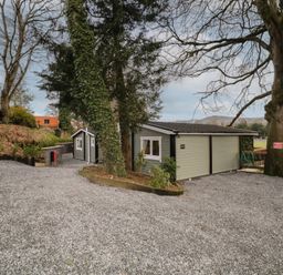 A gravel driveway with two small gray buildings surrounded by trees and a wooden fence at Owenbeg in Dungiven Londonderry