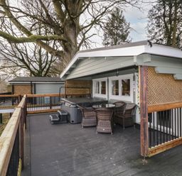An outdoor deck area with a hot tub wicker chairs and a round table surrounded by trees at The Castle in Dungiven Londonderry