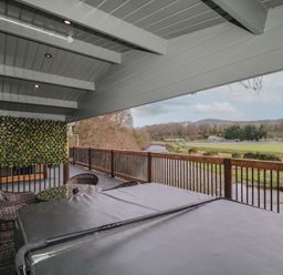 A covered balcony with a hot tub table and chairs overlooking a river and grassy field at The Castle in Dungiven Londonderry