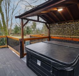 A covered deck with a hot tub and wooden railing overlooking trees at Hazel in Dungiven Londonderry