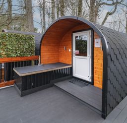 An outdoor wooden pod with a white door and black shingled roof surrounded by trees at Juniper in Dungiven Londonderry