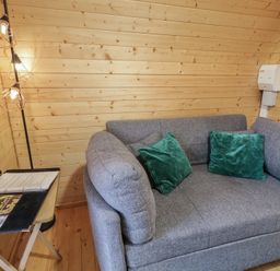 A corner of a room with a grey sofa with green cushions and a small table holding papers and a remote control at Juniper in Dungiven Londonderry
