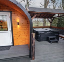 An outdoor wooden deck area with a covered hot tub and a small cabin with a white door at Birch in Dungiven Londonderry