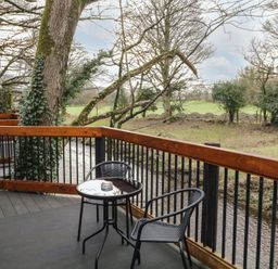 A balcony with a small round table and two chairs overlooking a creek and trees at Birch in Dungiven Londonderry