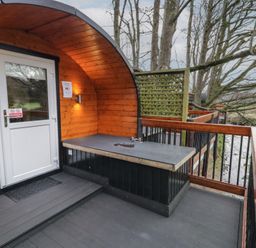 A wooden pod with a white door on a deck with a countertop and railing by a river at Yew in Dungiven Londonderry