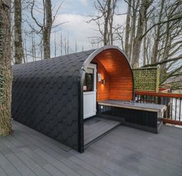 An outdoor pod with a black hexagonal roof and wooden interior on a deck with railing and trees nearby at Yew in Dungiven Londonderry