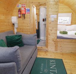 A wooden cabin interior with a gray sofa with green pillows a bed with folded towels and a shower enclosure at Yew in Dungiven Londonderry