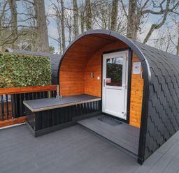 An outdoor pod cabin with wooden walls a white door and a black tiled curved roof on a grey deck with trees in the background at Elm in Dungiven Londonderry