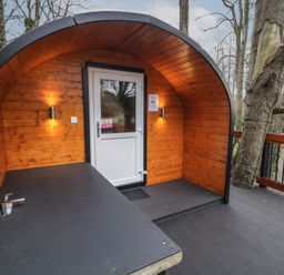 A wooden pod with a white door and bench under curved roof surrounded by trees at Elm in Dungiven Londonderry