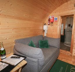 A small wooden room with a gray sofa with two green pillows a wooden side table with a bottle and papers a door leading to a bathroom with a shower at Elm in Dungiven Londonderry