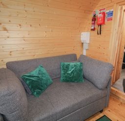 A gray sofa with two green pillows in a wooden room next to a small bathroom at Hawthorn in Dungiven Londonderry