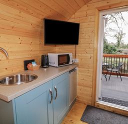 A kitchen area with a sink microwave coffee maker small fridge and a door leading to a balcony with chairs at Hawthorn in Dungiven Londonderry