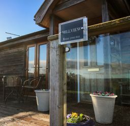 A wooden porch with glass doors, outdoor chairs, tables, and flower pots at Hillview in Stottesdon near Cleobury Mortimer