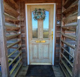 A wooden front door with a wreath on it and a black doormat on a wooden porch at Hillview in Stottesdon near Cleobury Mortimer