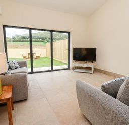 A living room with grey sofas a television on a stand and a lamp on a wooden side table at Bears Court Barn 3 Little Rissington near Bourton-On-The-Water