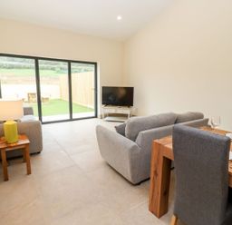 A living room with sofas television a dining table and glass doors leading to a garden at Bears Court Barn 3 Little Rissington near Bourton-On-The-Water
