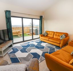 A living room with orange sofas a blue and gray geometric rug a television and sliding glass doors at Bears Court Barn 4 Little Rissington near Bourton-On-The-Water