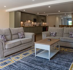 A living room with two gray sofas a wooden coffee table and a kitchen with green cabinets in the background at Bears Court Barn 7 Little Rissington near Bourton-On-The-Water