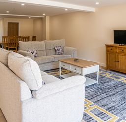 A living room with two sofas a coffee table a wooden TV stand with a television and a dining table with chairs at Bears Court Barn 7 Little Rissington near Bourton-On-The-Water
