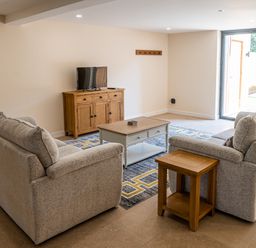 A living room with two sofas a coffee table a wooden cabinet with a television and sliding glass door at Bears Court Barn 7 Little Rissington near Bourton-On-The-Water
