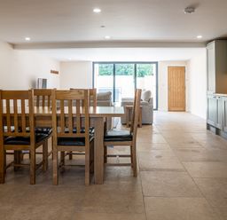 An open living space with a wooden dining table and chairs a seating area with sofas large windows and kitchen cabinets at Bears Court Barn 7 Little Rissington near Bourton-On-The-Water