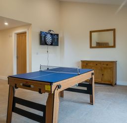A game room with a ping pong table a dartboard mounted on the wall a wooden door a wooden cabinet with drawers and a mirror above it at Bears Court Barn 8 Little Rissington near Bourton-On-The-Water