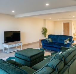 A living room with green and blue sofas a television on a white stand and a plant at Bears Court Barn 5 in Little Rissington near Bourton-On-The-Water