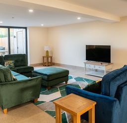 A living room with green and blue sofas a wooden side table and a television on a TV stand at Bears Court Barn 5 Little Rissington near Bourton-On-The-Water