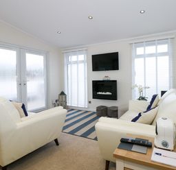 A living room with white sofas a wall-mounted TV and a fireplace at Un Diwrnod One Day The Warren T22 The Warren near Abersoch