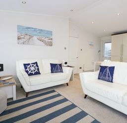 A living room with white sofas and blue nautical cushions at Un Diwrnod The Warren T22 The Warren near Abersoch