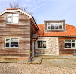 A wooden house with tiled roof gravel driveway and potted plants at Natterjacks in Syderstone