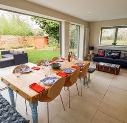 A dining area with a wooden table set for six and a living room with a blue sofa and cushions at Natterjacks in Syderstone