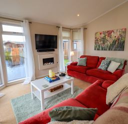 A living room with red sofas a white coffee table a wall-mounted tv and large windows overlooking water at Otters Reach near Carnforth