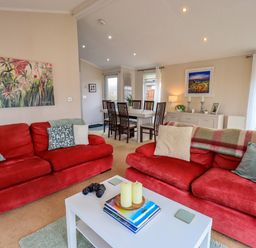 A living room with two red sofas and a white coffee table by a dining area at Otters Reach near Carnforth