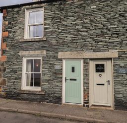 Stone exterior wall with two windows and two doors of cottages named Capella Cottage and Brock Cottage in Keswick