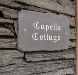 A stone wall with a sign reading Capella Cottage next to a green door at Capella Cottage in Keswick