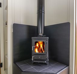 A wood burning stove with fire inside in a corner with black paneling at Blackthorn South Leigh near Witney