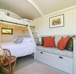 A small room with a bunk bed a wicker chair and a cushioned bench with pillows at Blackthorn South Leigh near Witney