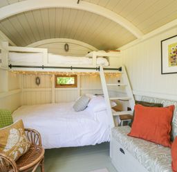 A bedroom with bunk beds a wicker chair with a cushion a small sofa with orange pillows and a painting on the wall at Blackthorn in South Leigh near Witney