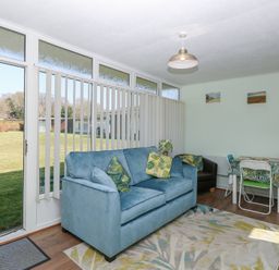 A living room with a blue sofa green pillows a black armchair dining table with chairs and large windows at Number 19 in Cromer