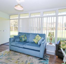 A living room with a blue sofa and patterned cushions near a window with vertical blinds at Number 19 in Cromer