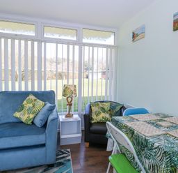 A sitting area with blue sofa and black chair with leaf patterned cushions next to a table with leaf patterned tablecloth at Number 19 in Cromer
