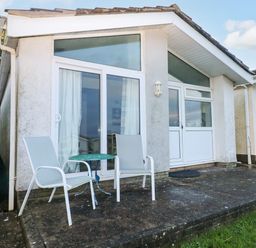 A patio area with two chairs and a small round table outside a bungalow with large windows and a door at Chalet 27 in Port Eynon