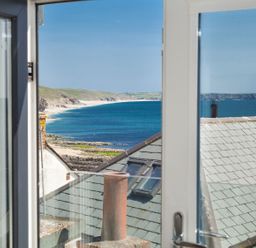 View of a beach and coastline through an open window with rooftops in the foreground at The Loft in Porthleven
