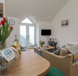 A living room with a beige sofa a wooden coffee table a tv mounted on the wall and glass doors with a sea view at The Loft in Porthleven