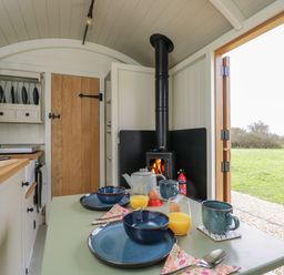 A small kitchen with a wood stove a table set for breakfast and an open door showing grass outside at Hazel South Leigh near Witney